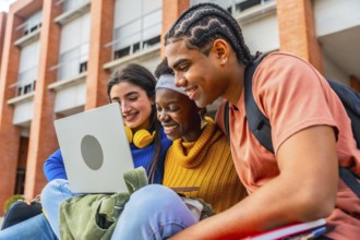 Group of happy young diverse students collaborating on a project, smiling and looking at a laptop