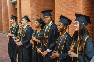 Diverse group of young students and graduates wearing academic regalia or cap and gown, smiling and