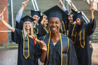 Happy young graduates in caps and gowns smiling and celebrating together on campus, holding