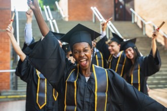 Smiling young woman posing with raised arms and holding a diploma while celebrating her academic