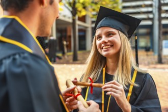 Smiling university graduate in cap and gown accepts rolled diploma from unseen hand, celebrating