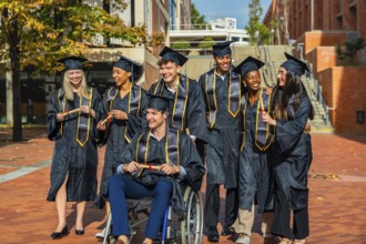 Group of smiling diverse students wearing graduation caps and gowns, holding diplomas and