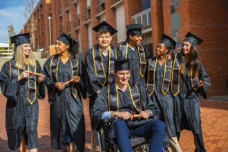 Diverse group of young adult students wearing academic gowns and mortarboards, holding diplomas and