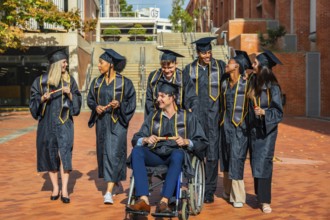 Diverse group of university graduates, including a man in a wheelchair, standing together on campus