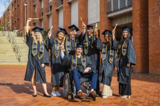 Group of happy multiracial university students wearing graduation caps and gowns, holding diplomas,