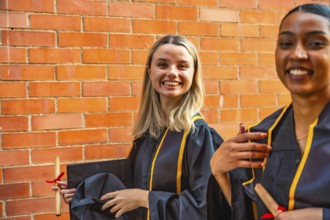 Diverse young women celebrating graduation, smiling brightly while wearing academic gowns and