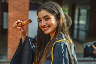 Smiling young woman celebrating graduation, proudly holding her rolled up diploma, wearing a cap