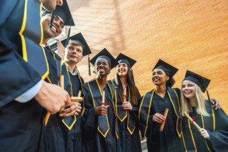 Diverse students wearing graduation gowns and caps, smiling while holding diplomas, celebrating