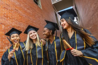 Four happy diverse university graduate students wearing academic caps and gowns, celebrating their