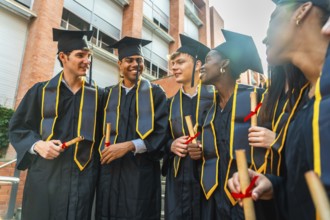 Group of diverse graduating students wearing academic gowns and caps, smiling while holding their