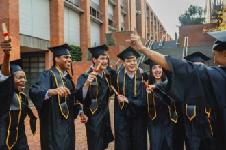 Diverse group of young students wearing graduation caps and gowns, holding diplomas, and happily