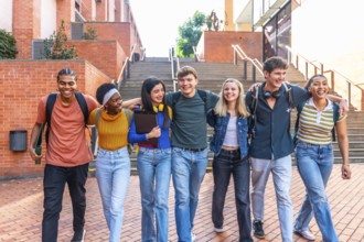 Diverse group of happy young adult university students walking arm in arm after classes on campus,