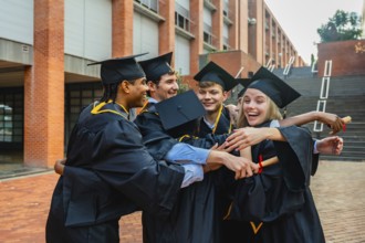 Group of excited young multi ethnic alumni students wearing academic dresses and cap, hugging,