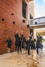 Group of happy diverse university graduates throwing their academic caps into the air and jumping