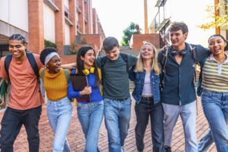 Group of happy diverse university students with backpacks embracing shoulders, laughing and walking