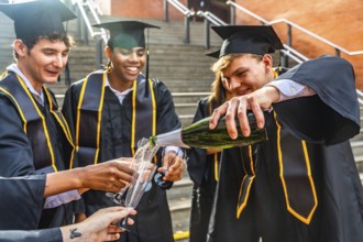 Diverse group of university students wearing black graduation caps and gowns celebrating with