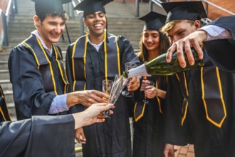 Diverse group of happy university graduates wearing academic dress and caps, receiving champagne