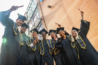 Group of smiling multi ethnic university students wearing graduation caps and gowns, happily