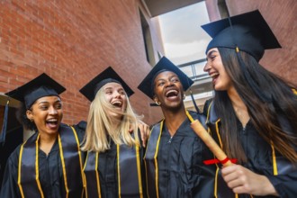 Group of happy diverse female university graduates wearing caps and gowns, laughing joyfully