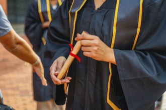 Graduate student is holding a rolled diploma tied with a red ribbon, celebrating academic
