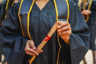 Graduate student is proudly holding a rolled diploma tied with a red ribbon, celebrating academic