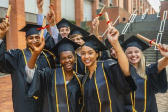 Group of happy young university graduates wearing academic dress and caps, raising diplomas in