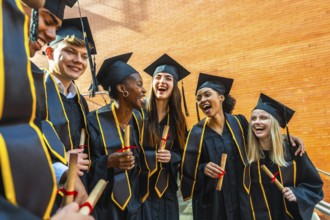 Diverse group of smiling students celebrating their graduation, wearing cap and gowns, holding