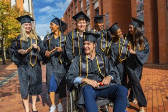 Diverse group of university graduates, including a man in a wheelchair, smiling and holding
