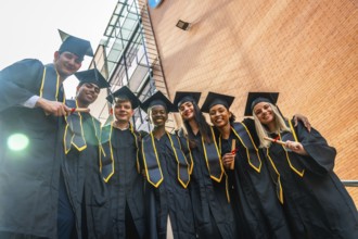 Diverse group of joyful university graduates in caps and gowns standing outdoors by campus
