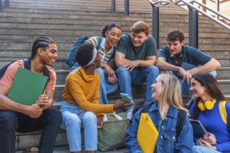 Group of young multi ethnic students sitting on steps, laughing and looking at a smartphone,