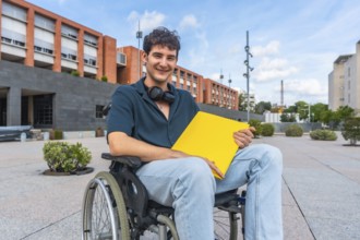Young male student in a wheelchair smiling, holding a yellow folder, and wearing headphones around