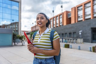 Young latina student smiling and walking on a university campus while carrying a backpack and a red