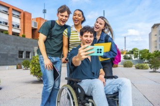 Group of happy young university students, including a man in a wheelchair, smiling and laughing