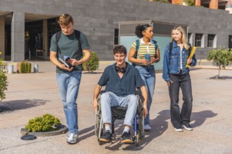 Group of four diverse university students walking on campus outdoors, one young man in a wheelchair