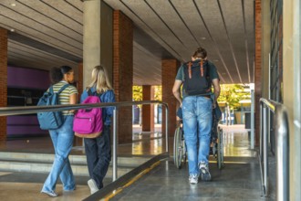 University students walking up an accessible campus ramp, one friend pushing another in a