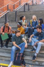 Diverse group of university students sitting on urban campus stairs, chatting, studying and