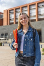 Happy young blonde woman with a backpack and a red folder, smiling confidently while standing