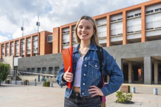Happy young female student with backpack and folder smiling, standing in front of a modern