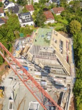 Construction site with partially erected roof, crane and neighboring houses in a residential area,