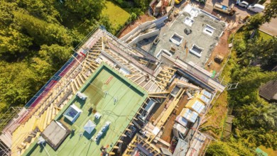 Aerial view of a construction site with roof structures and materials in a green environment,