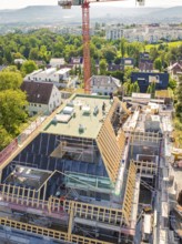 Construction of a multi-storey building with crane and scaffolding in a green urban environment,