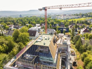 View from above of a construction site with crane and surrounding residential buildings and trees,