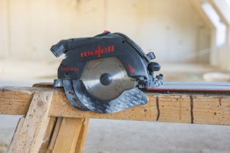 Close-up of a black and red circular saw on a wooden table, carpentry construction, roof extension,