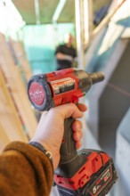 A worker holds a red electric screwdriver in a construction site situation, carpentry construction,