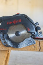 Close-up of a black and red circular saw on a wooden table, carpentry construction, roof extension,