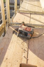 An electric drill is lying on wooden planks of scaffolding under bright sunlight, carpentry