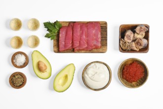 Colorful ingredients on a white surface, including sliced salted tuna, canned tuna, avocado, red