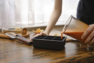 A person is pouring a blend of sea buckthorn, orange and ginger into a silicone ice tray on a