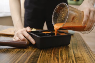 A person pours a blend of orange, sea buckthorn and ginger from blender container into a silicone