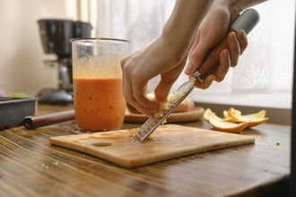 A person is grating fresh ginger on a wooden cutting board in a kitchen. There is a blender with